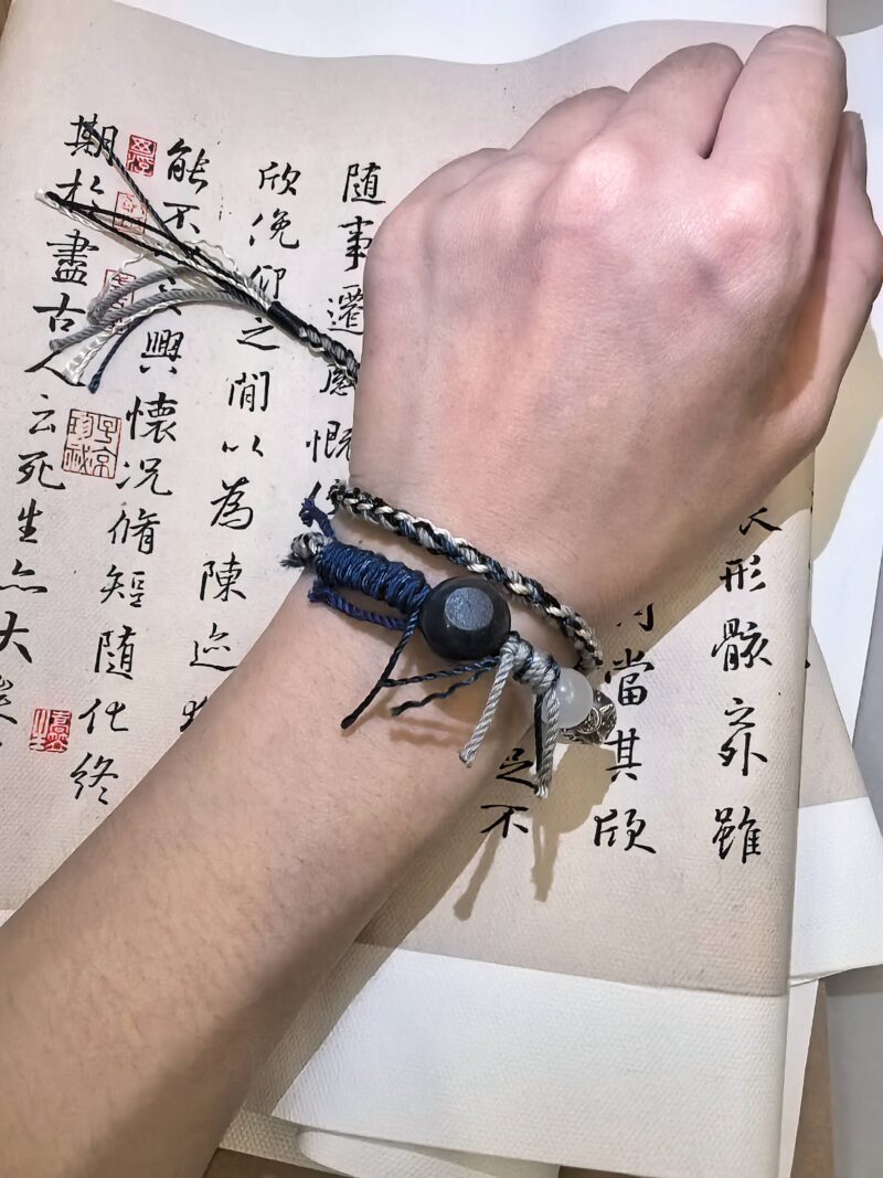 Auspicious bracelet from EBIG Jewel on wrist held against writing.